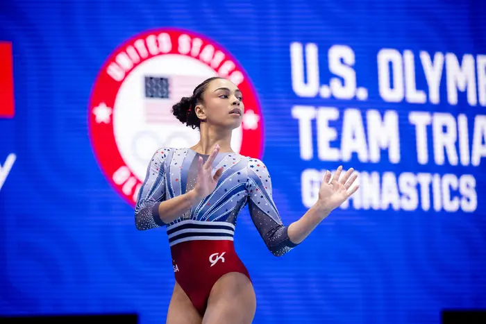 A gymnast poses in front of a blue wall.